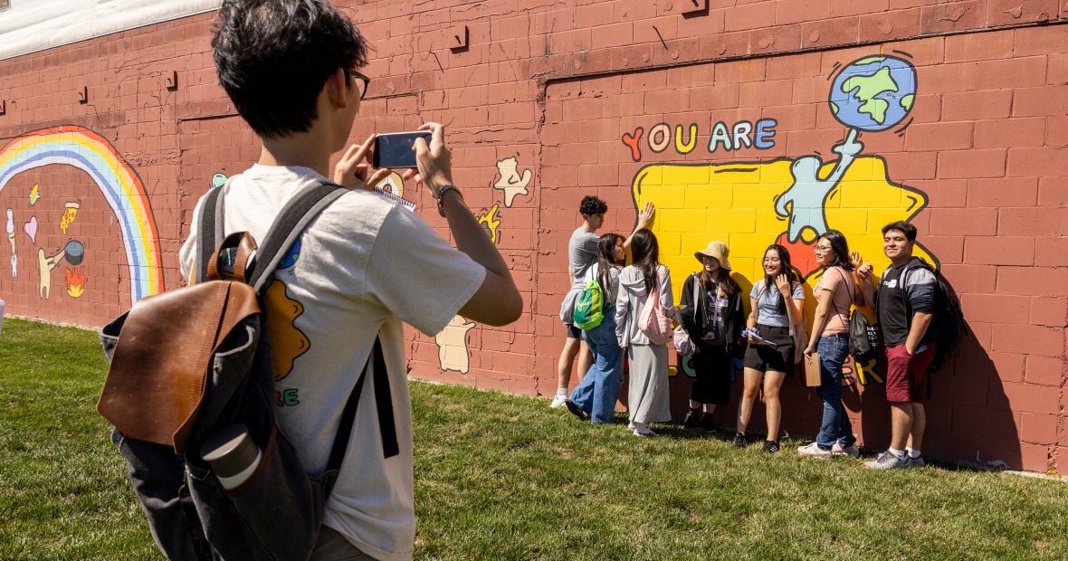 people pose in front of an outdoor wall mural
